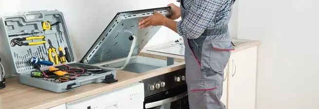 Cooktop repair technician lifting a built-in stovetop for service in Cambridge, MA