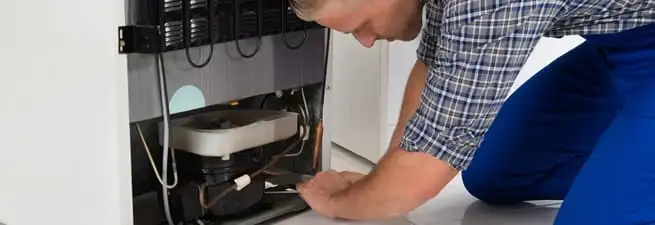 Refrigerator repair technician servicing the compressor and condenser area in Cambridge, MA