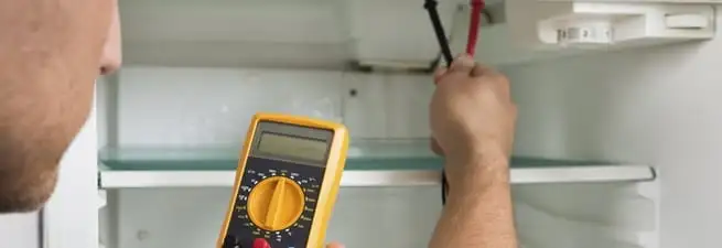 Refrigerator repair technician testing electrical components with a multimeter in Cambridge, MA