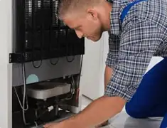 Refrigerator repair technician servicing the compressor and condenser area in Cambridge, MA